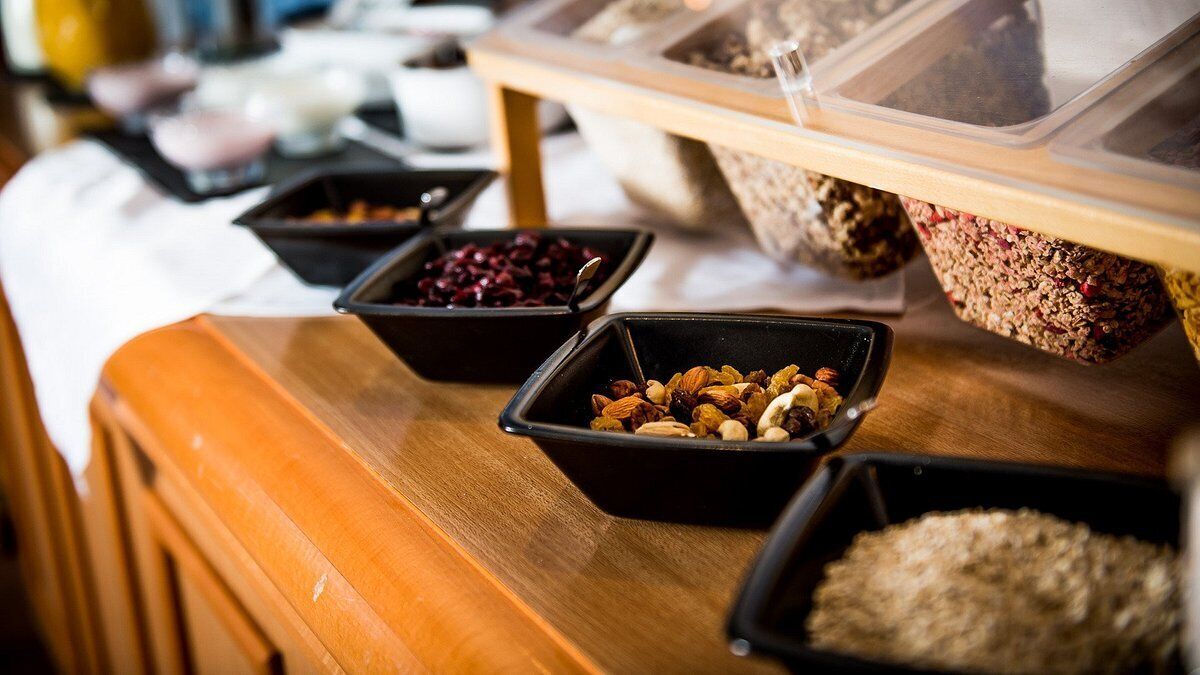 Mesa de buffet com diversos alimentos em tigelas pretas, incluindo nozes, frutas secas e cereais.