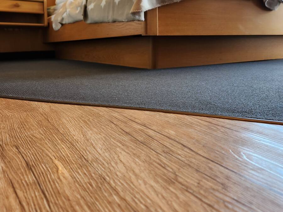 Una cama de madera con una manta gris, una mesita de noche con una lámpara y un cuadro enmarcado en la pared.
