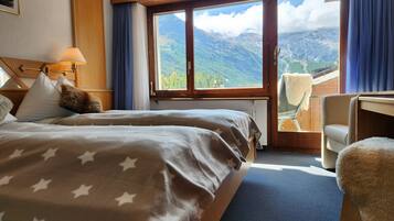 Habitación de hotel con dos camas, un ventanal con vistas a la montaña, una silla y una mesita.