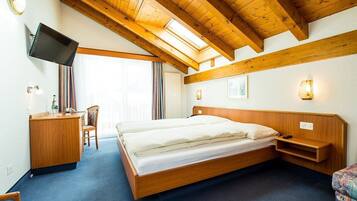 Habitación de hotel con techo de madera, cama, escritorio, silla, televisión y ventana.