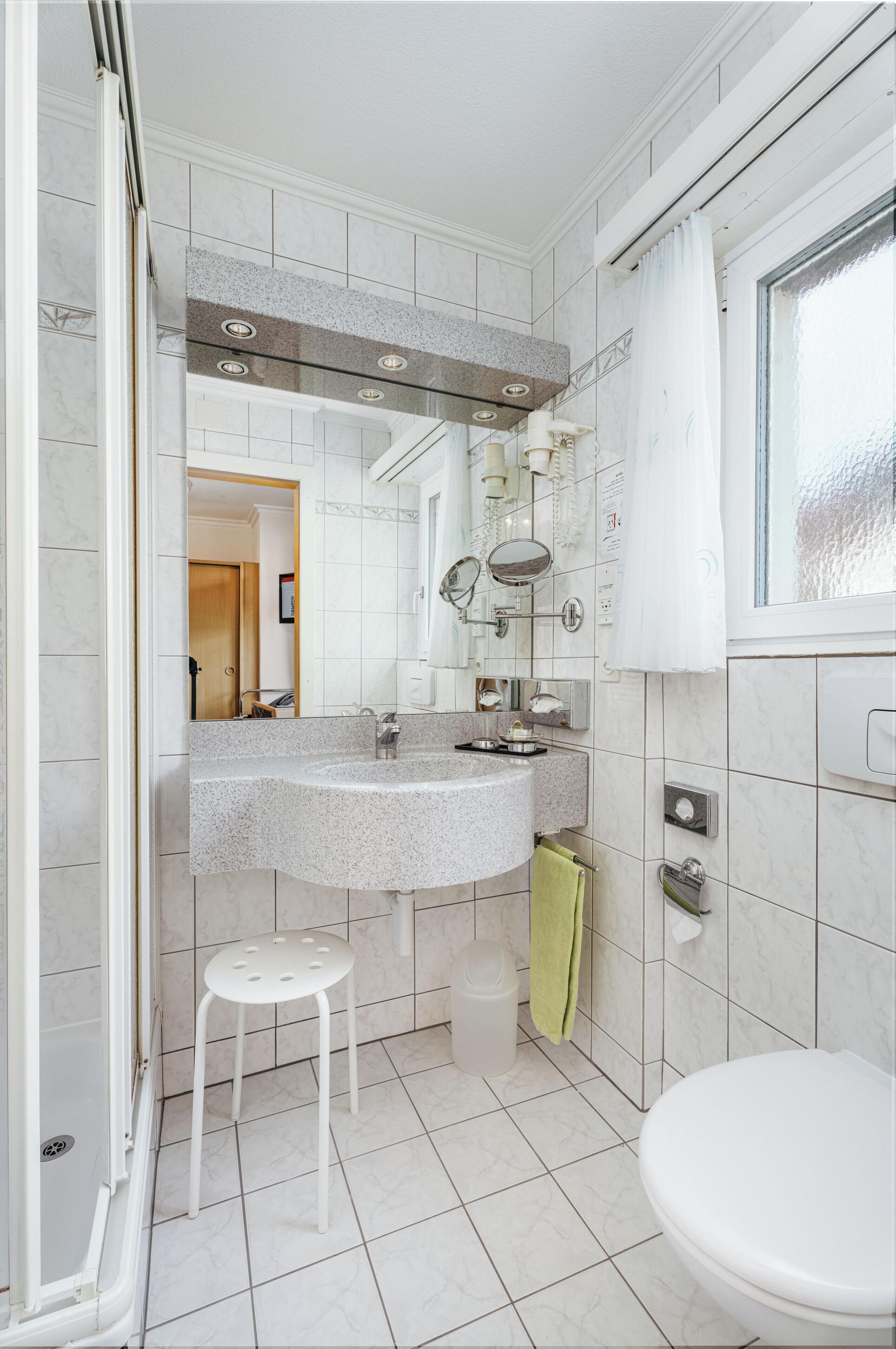 Une salle de bain avec des toilettes blanches, un lavabo avec un miroir et un espace douche.