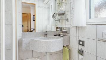 Une salle de bain avec des toilettes blanches, un lavabo avec un miroir et un espace douche.