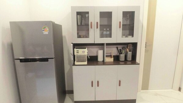 Cocina compacta con refrigerador, cafetera y armarios de vidrio.