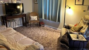 A living room with a television, a piano, a chair with a cushion, a lamp, and a couch. - Charming 2-bedroom house with AC, WiFi, walking distance from UPTOWN! (Albuquerque)