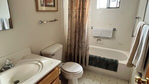 A bathroom with a sink, toilet, bathtub, and a window. - Charming 2-bedroom house with AC, WiFi, walking distance from UPTOWN! (Albuquerque)