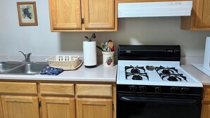 A kitchen with wooden cabinets, a stainless steel sink, a stove, and a white countertop. - Charming 2-bedroom house with AC, WiFi, walking distance from UPTOWN! (Albuquerque)