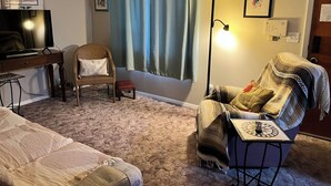 A living room with a television, a wicker chair, a sofa, a lamp, and a blanket. - Charming 2-bedroom house with AC, WiFi, walking distance from UPTOWN! (Albuquerque)