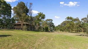 A large, open grassy area with a building featuring a wooden facade and a covered porch. - Metung Farmhouse set on 2 acres (Metung)