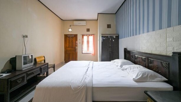 Habitación de hotel con cama, escritorio con televisor, armario y ventana con cortinas.