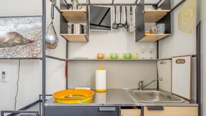 Een kleine keuken met een spoelbak, planken en een televisiescherm waarop een schildpad te zien is.