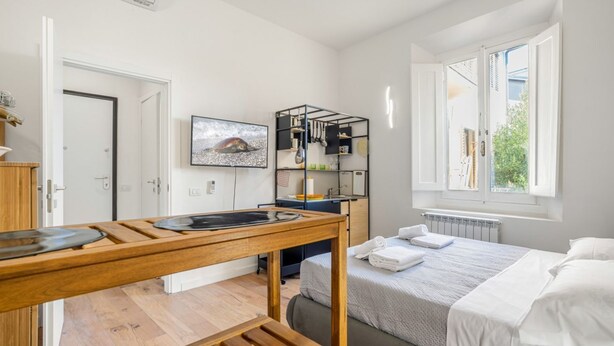 Een moderne hotelkamer met een bed, een houten tafel, een televisie en een plank met keukenbenodigdheden.