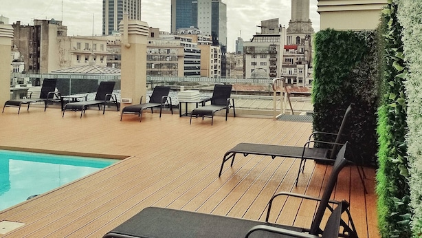 A rooftop pool area with lounge chairs and a view of the city skyline.
