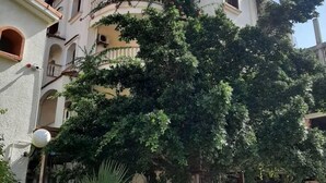 A multi-story building with balconies, surrounded by lush greenery and parked cars. - Hotel Plage d'or (Jijel)
