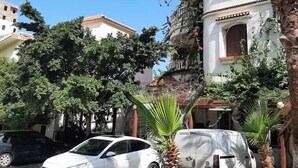 A residential area with a white car parked on the street, a white van, and a multi-story building with balconies. - Hotel Plage d'or (Jijel)