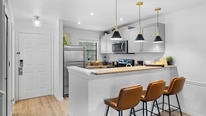 A modern kitchen with a central island, bar stools, stainless steel appliances, pendant lighting, and a white door. - Stop Scrolling - FREE Water Park Access - Newly Renovated Family Resort Home (Kissimmee)