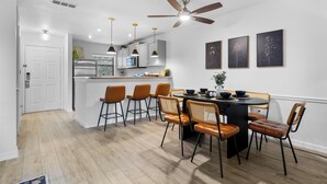A modern kitchen with white cabinets, a central island, and a dining area with wooden chairs. - Stop Scrolling - FREE Water Park Access - Newly Renovated Family Resort Home (Kissimmee)