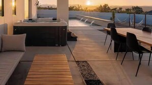 Un patio moderno al aire libre con jacuzzi, zona de estar y comedor con vistas al atardecer.