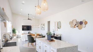 Une cuisine moderne dotée d’un grand îlot central, de luminaires suspendus et d’un coin repas avec une table et des chaises.