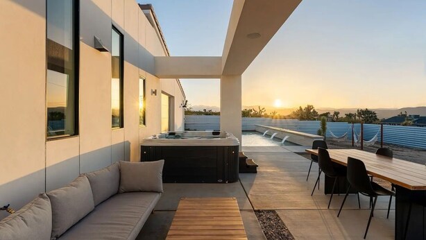Un patio moderno al aire libre con jacuzzi, zona de estar y comedor con vistas a un paisaje pintoresco.