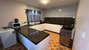 Una cocina compacta con una isla central, microondas, un refrigerador pequeño, estufa y una ventana con cortinas estampadas.