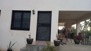 Una casa con puerta negra, dos ventanas con mosquiteras y varios maceteros con plantas en la fachada.