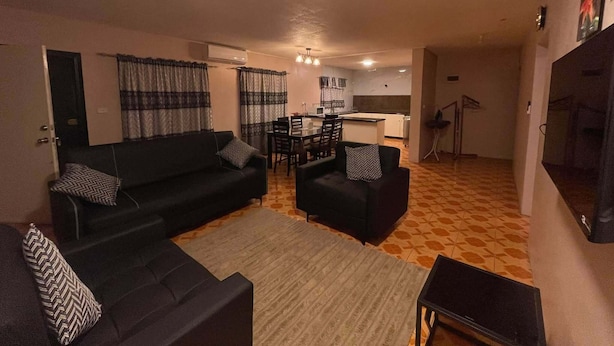 Una sala de estar con sofá, sillas, una mesa baja, una mesa de comedor y una cocina al fondo.