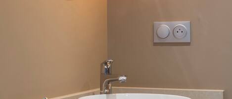A bathroom with a white sink, a round mirror with a light, and a glass container with toothbrushes.