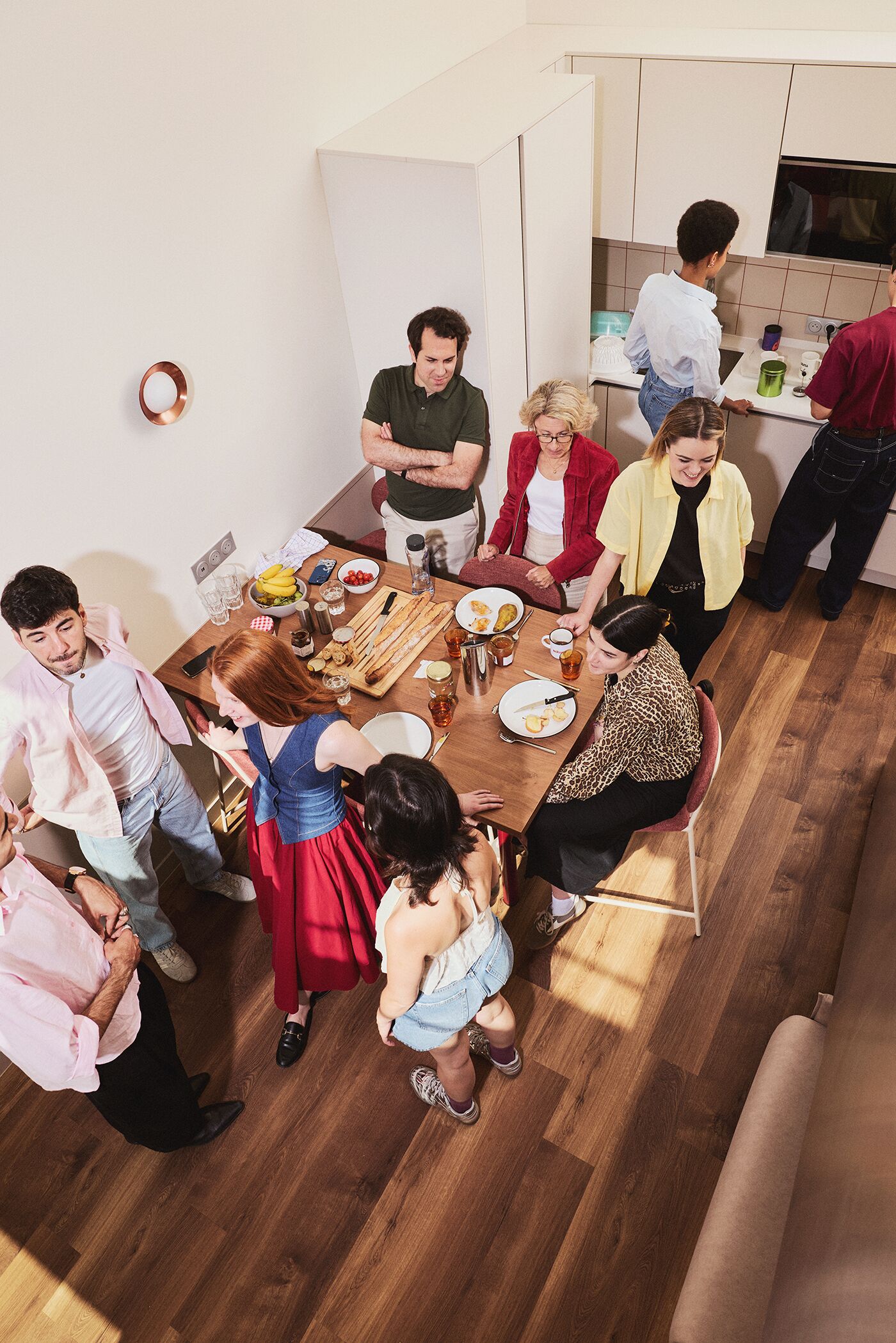 Un grupo de personas reunidas alrededor de una mesa de comedor en una habitación con piso de madera y paredes blancas.