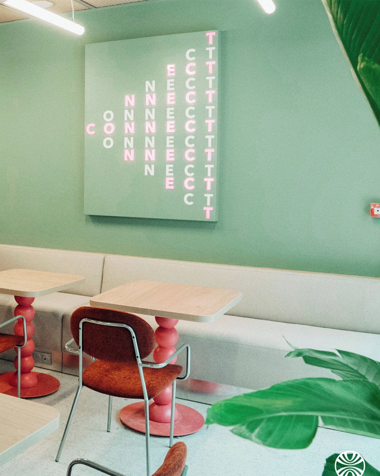 A seating area with tables and chairs, a wall with a vertical text display, and a large green plant.