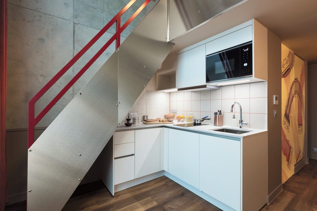 A modern kitchen with white cabinets, a microwave, and a red staircase.