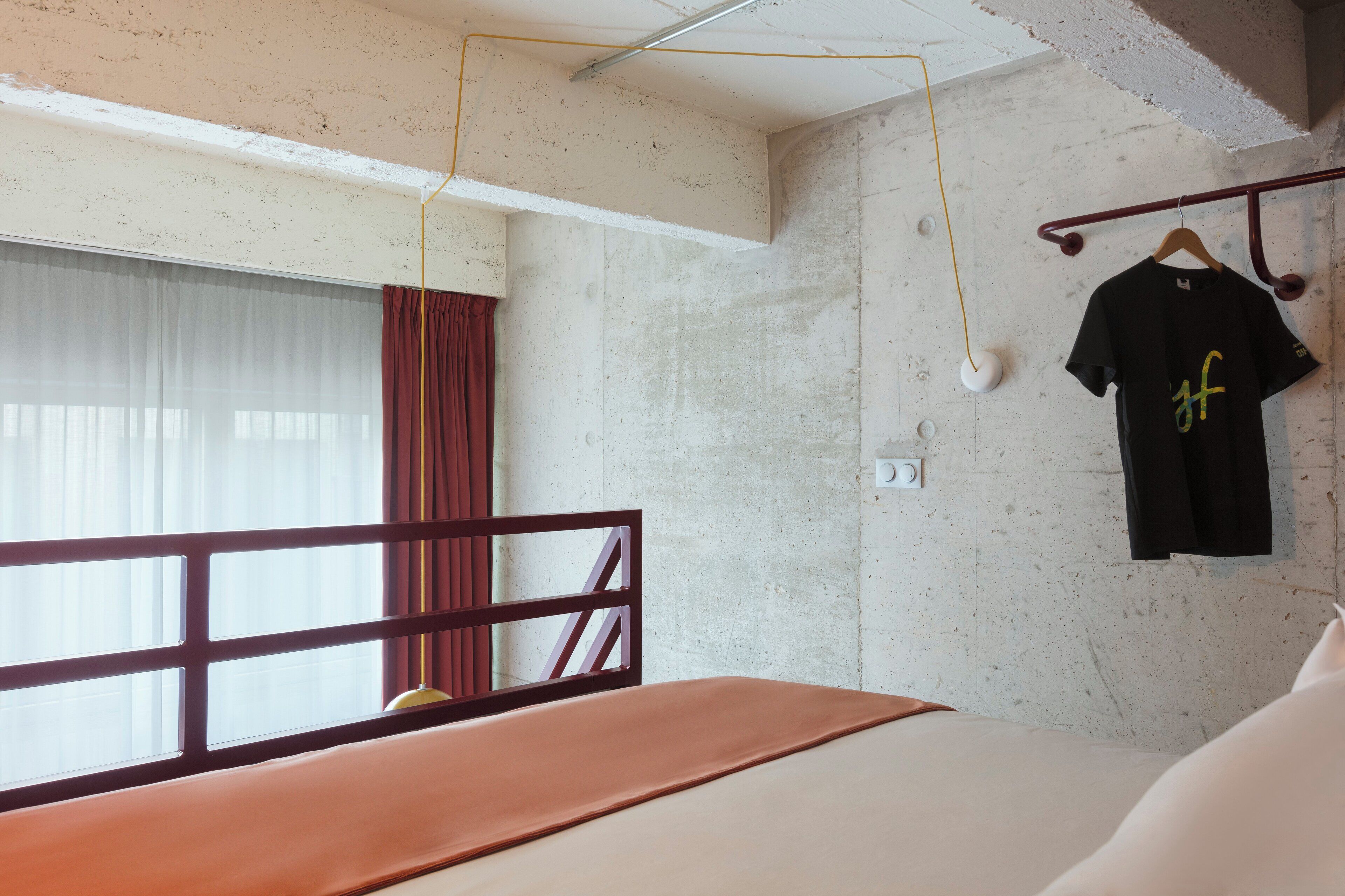 A bedroom with a bed, a window with curtains, a hanging light fixture, and a wall-mounted towel rack.