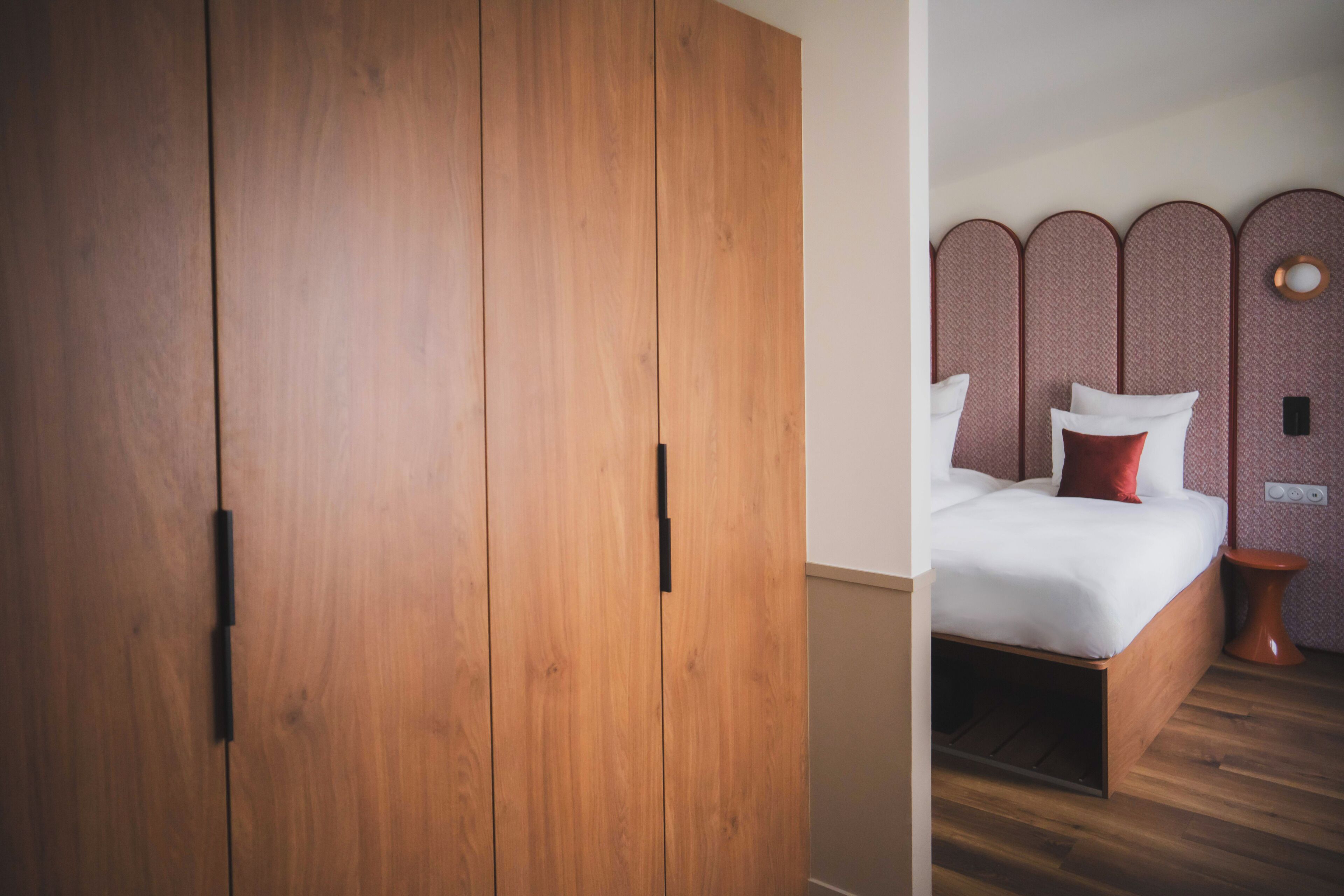 Une chambre avec une armoire en bois, un lit avec une literie blanche et un luminaire rond fixé au mur.