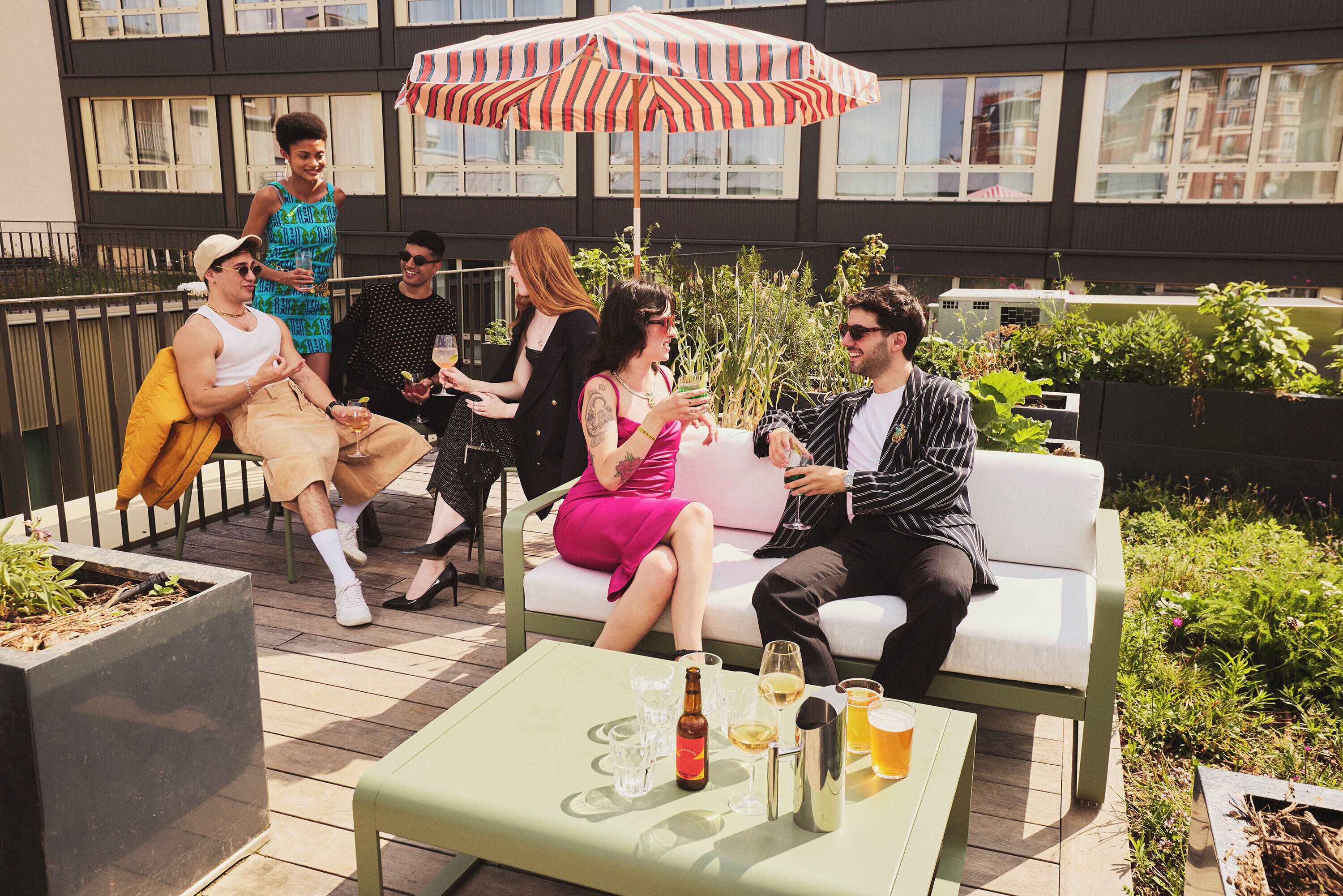 Un grupo de personas sentadas en mobiliario exterior, con bebidas sobre una mesa y una sombrilla proporcionando sombra.