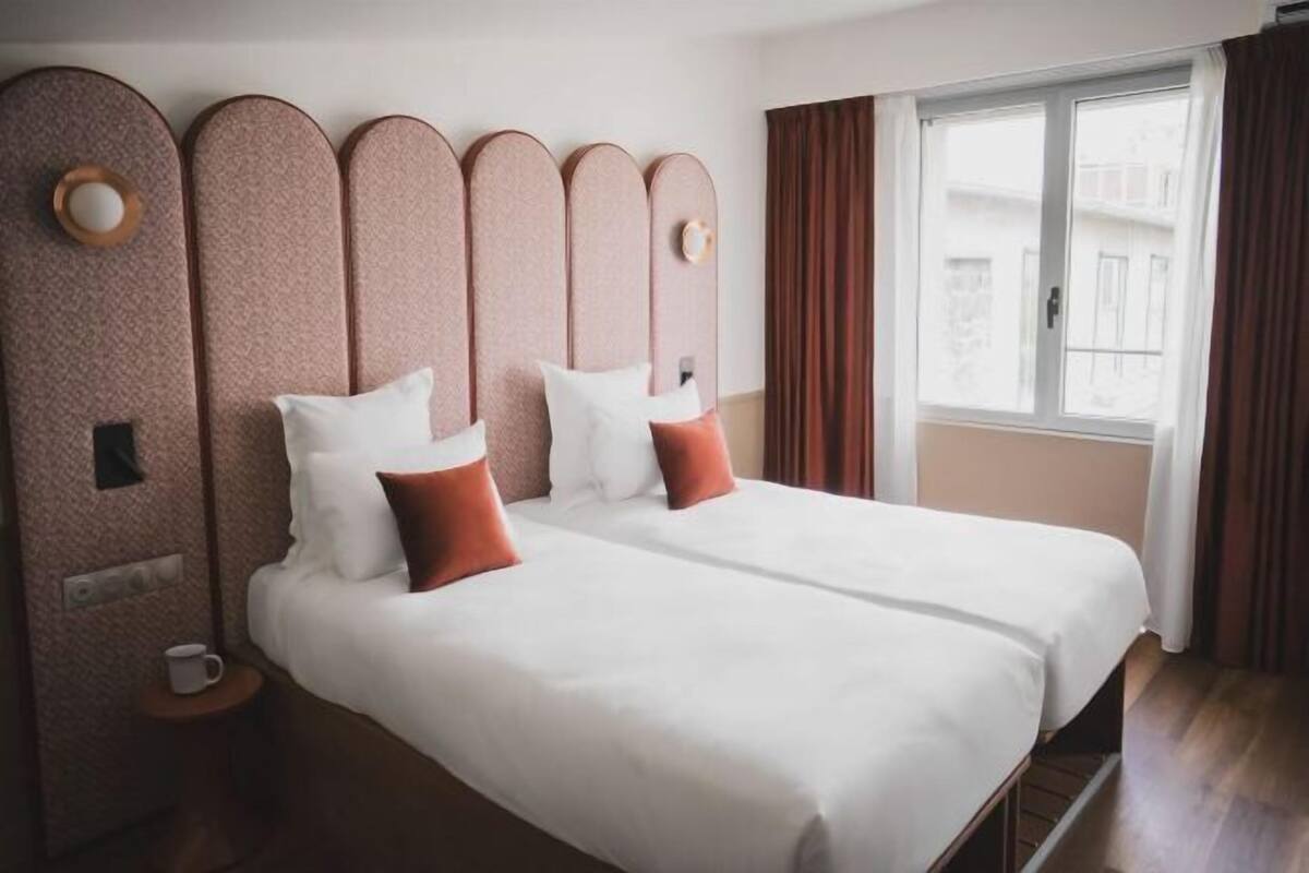 A double bed with a headboard, a bedside table with a cup, and a window with curtains.