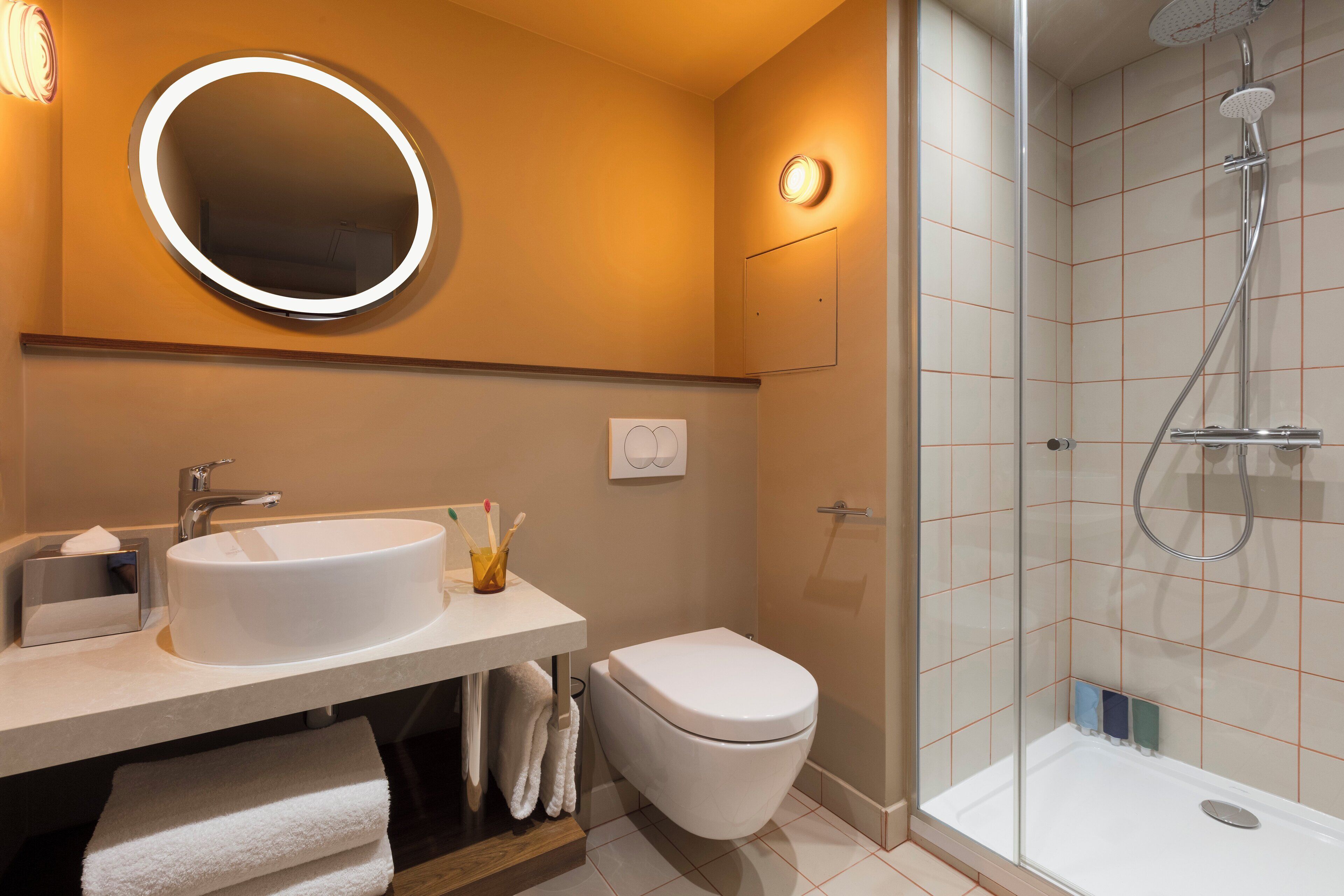 A modern bathroom with a round mirror, a sink, a toilet, and a glass-enclosed shower area.