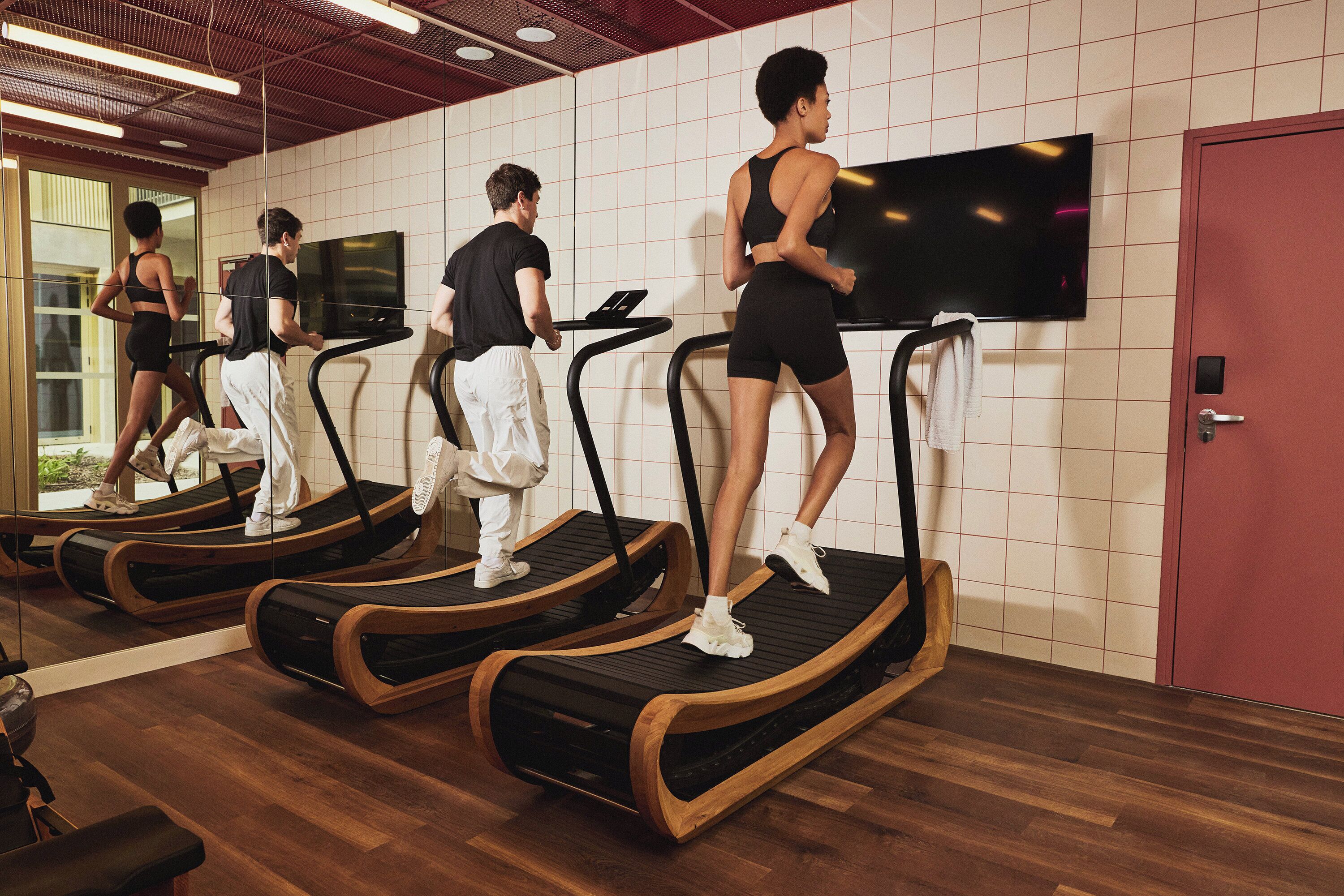 Et fitnessrum med løbebånd, et fjernsyn på væggen og trægulv.