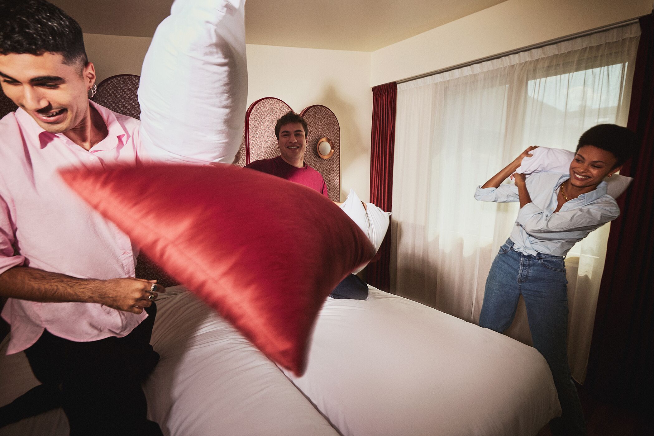 A hotel room with a bed, a headboard, and a window with curtains.