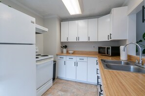Een kleine keuken met witte kastjes, een magnetron, een spoelbak en een fornuis.