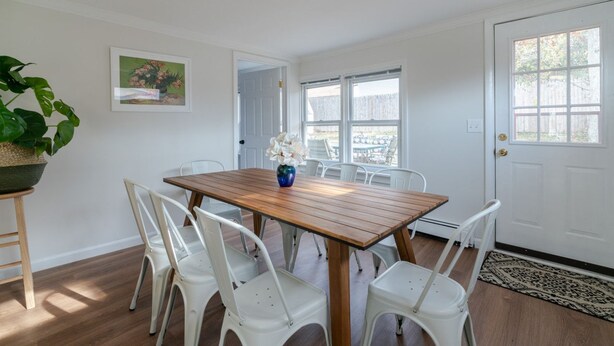 Un coin repas avec une table en bois et des chaises blanches, une plante en pot et un tableau accroché au mur.