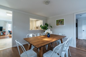 Un comedor con una mesa de madera y sillas blancas, un jarrón con flores y un cuadro en la pared.