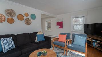 Ein Wohnzimmer mit einem schwarzen Sofa, blauen Sesseln, einem Couchtisch und einem Flachbildfernseher.