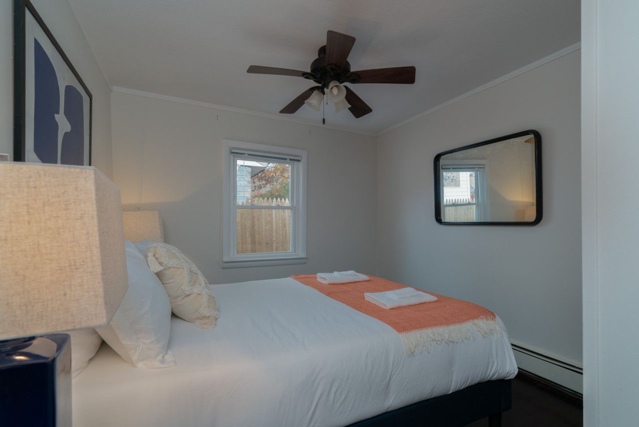 Ein Schlafzimmer mit Bett, Deckenventilator, Fenster und Spiegel an der Wand.