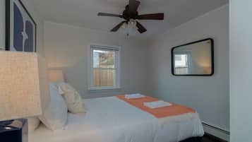Ein Schlafzimmer mit Bett, Deckenventilator, Fenster und Spiegel an der Wand.