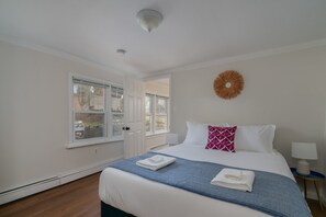 Une chambre d’hôtel avec un lit, une fenêtre, un élément décoratif sur le mur et une table de chevet.