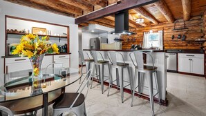 A modern kitchen with a wooden ceiling, a glass dining table, and bar stools.