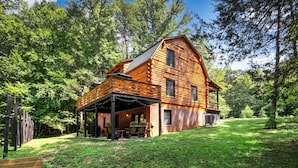 A log cabin with a covered patio and a small deck, surrounded by a forest.