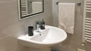Et badeværelse med en hvid vask, et spejl, et håndklædetørrestativ og et toilet.