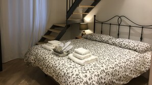 Et soveværelse med en seng, et natbord, en lampe, et vindue med gardiner og en trætrappe.