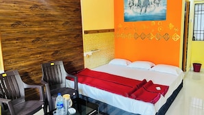 A hotel room with a wooden wall, a bed with white and red bedding, a painting of horses, and a small table with chairs and water bottles.