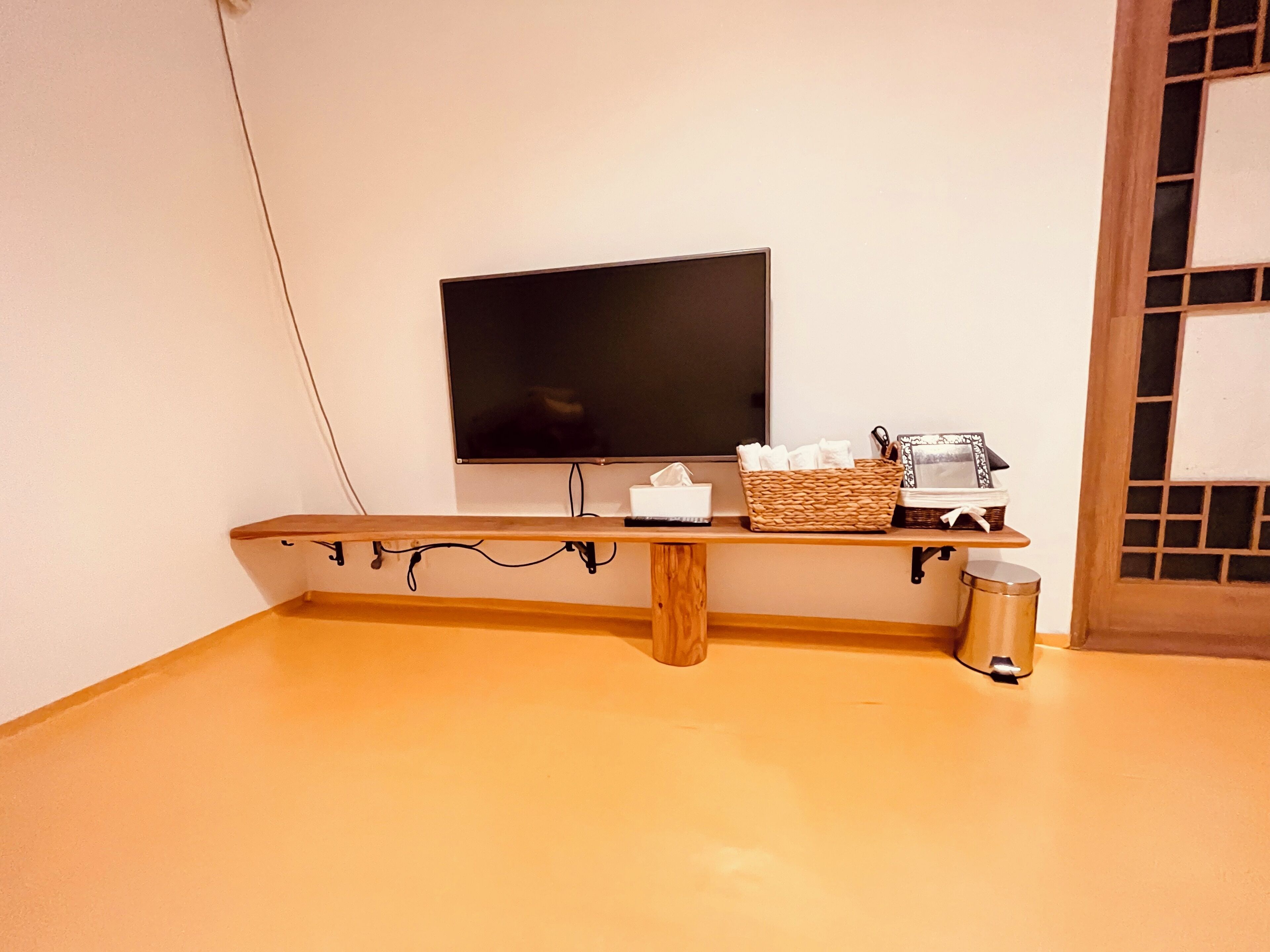 A room with a wooden bench, a television mounted on the wall, a basket with tissues, and a trash bin.